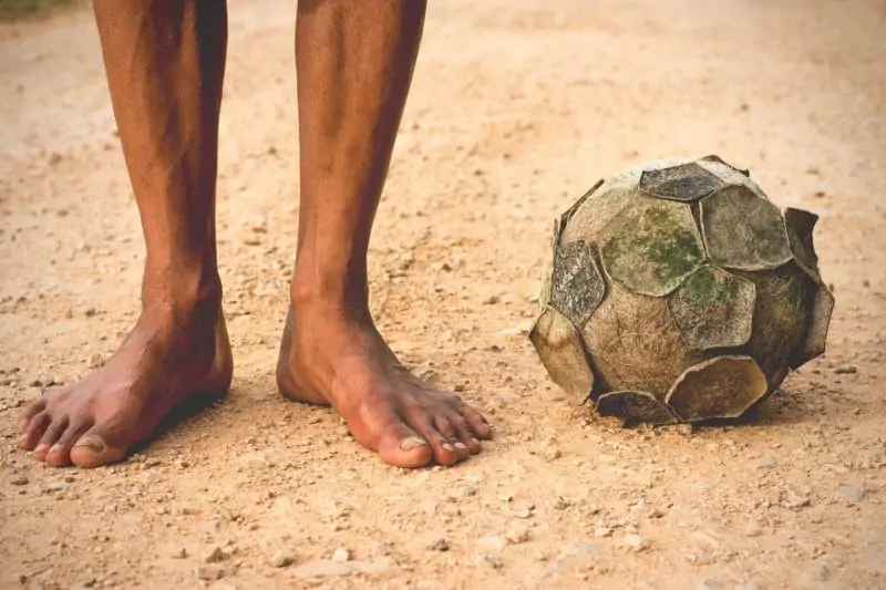 old soccer ball The legs of a man standing with a soccer ball on a dirt old, vintage tone.