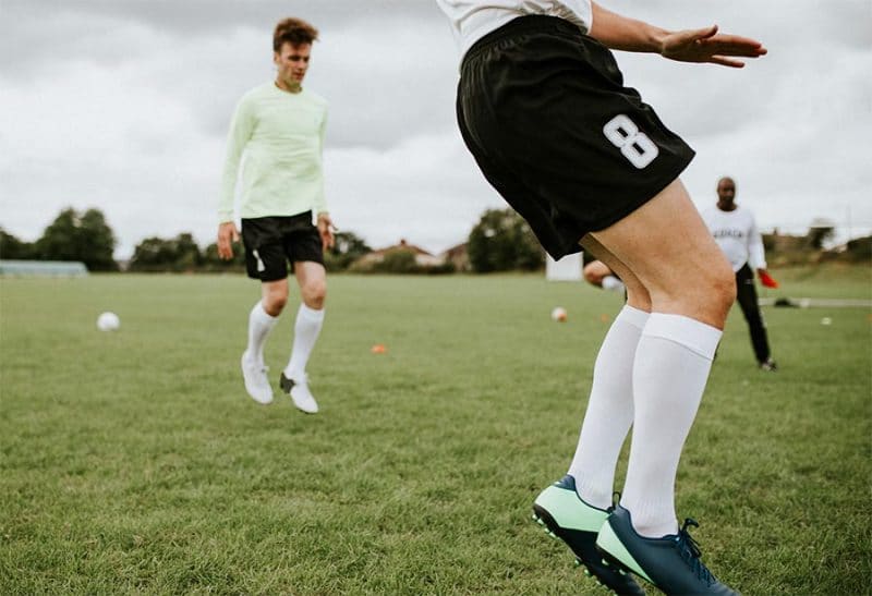 Soccer player on toes showing cleats socks shorts with player behhind