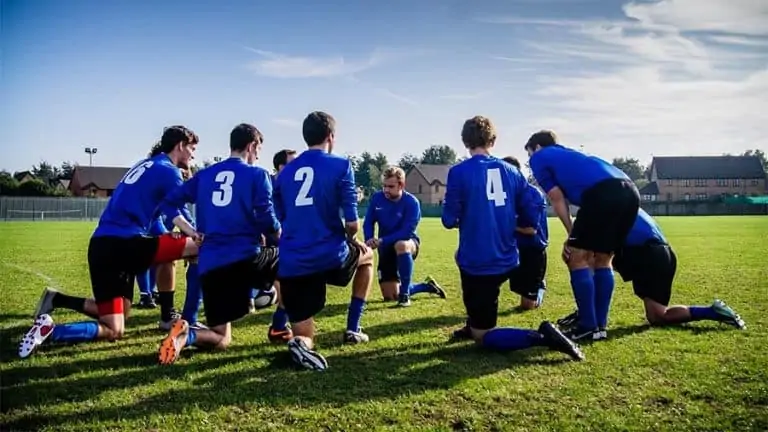 Soccer team on their knees on a field e1578134437353