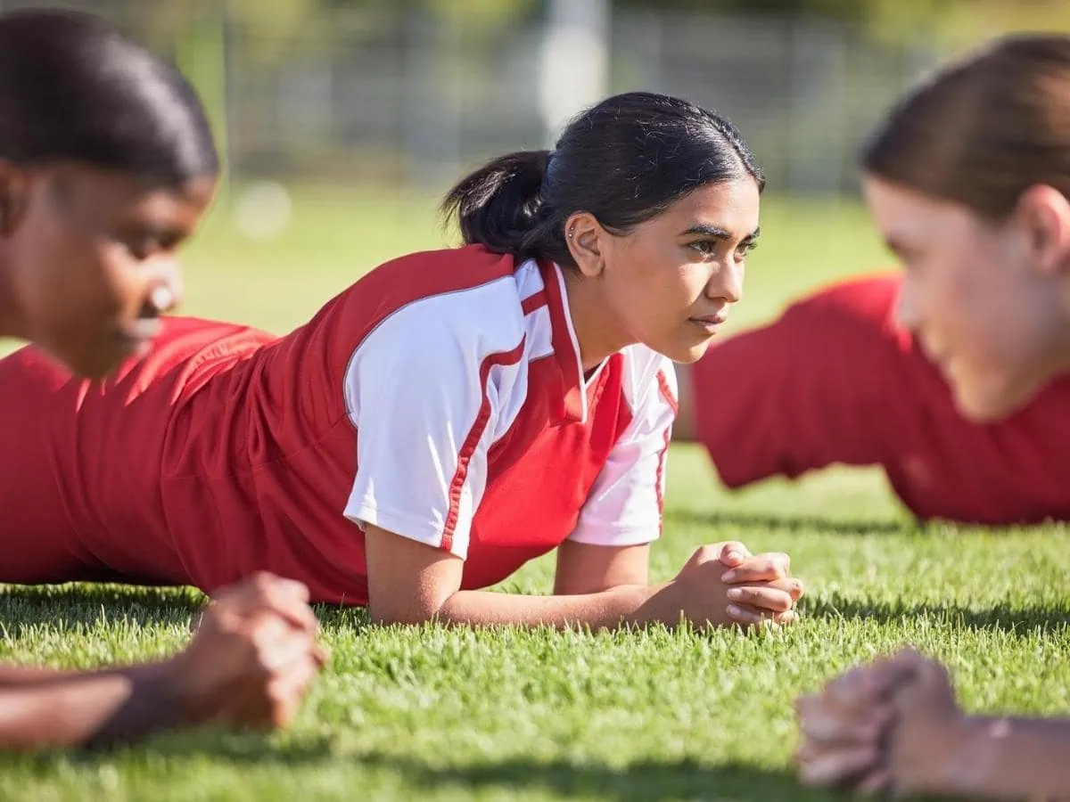Women soccer players in a team doing the plank fitness exercise in training together on a practice sports field. ○ Soccer Blade
