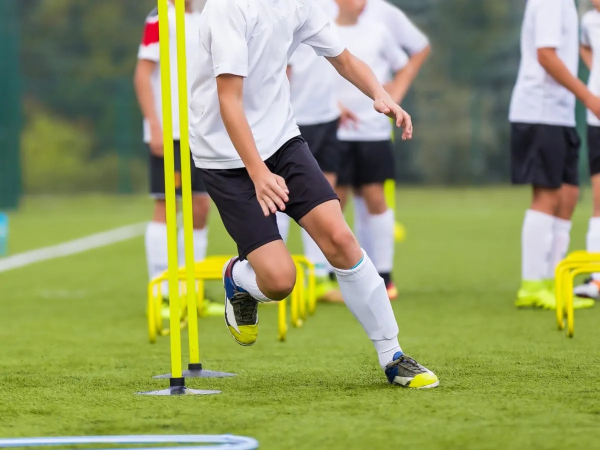 Soccer Player In Training during camp. Boy Running Between Cones During Practice in Field on Sunny Day. Young Soccer Players at Speed and Agility Practice Session. ○ Soccer Blade