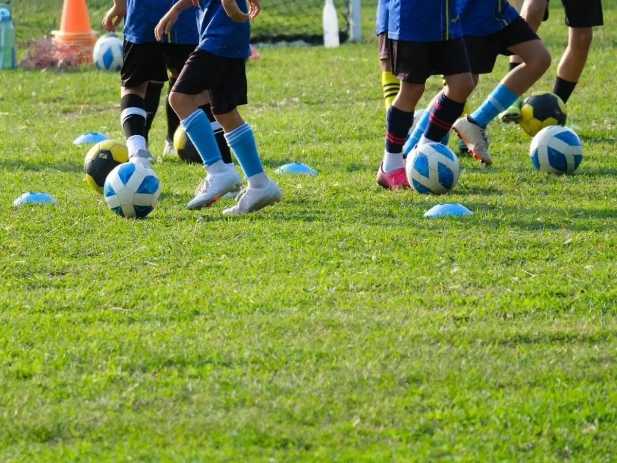 Group of school children running and kicking soccer balls on grass field. Kids practicing football on summer training camp close up. ○ Soccer Blade