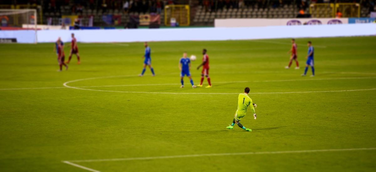 Soccer goalkeeper kicks out the ball during the match at stadium. Ball mid flight. ○ Soccer Blade