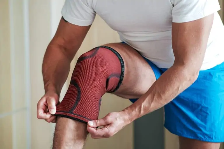 A man puts a sports knee pad on an injured knee before training