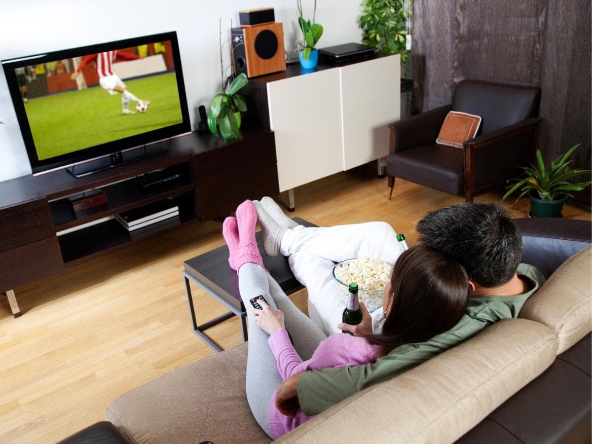 Couple watching soccer on TV while relaxing on a sofa. ○ Soccer Blade