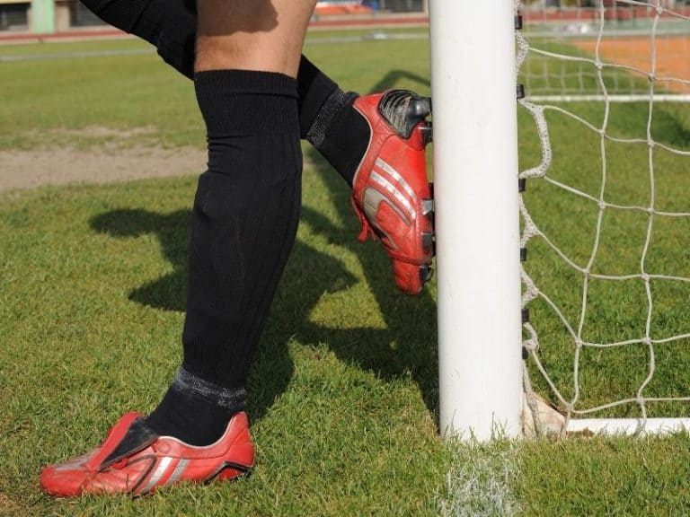 Goalies legs and feet standing next to a soccer goal