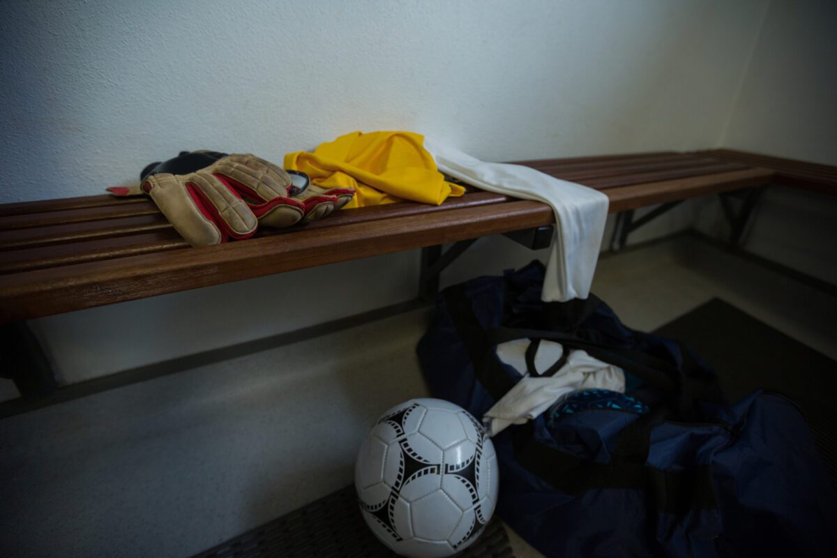 Gloves with football jersey soccer ball and travel bag on bench in changing room. ○ Soccer Blade