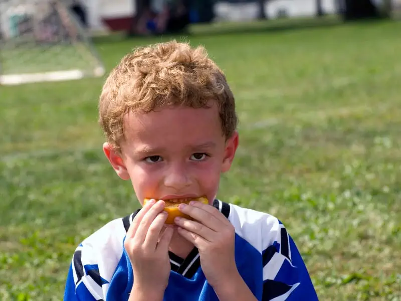 young soccer player eats orange slice