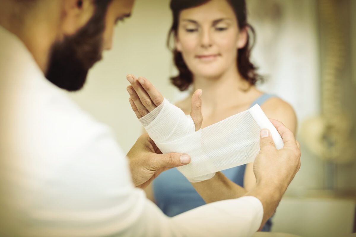 Physiotherapist putting bandage on injured hand of patient in clinic ○ Soccer Blade