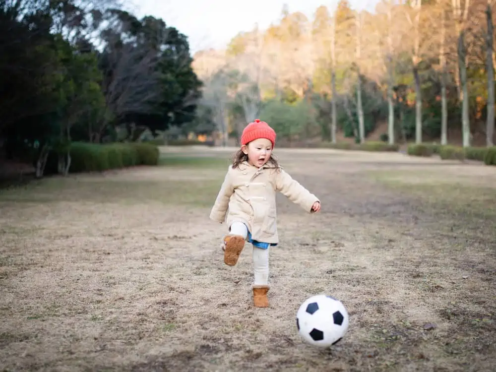 young girl in winter clothes playing soccer