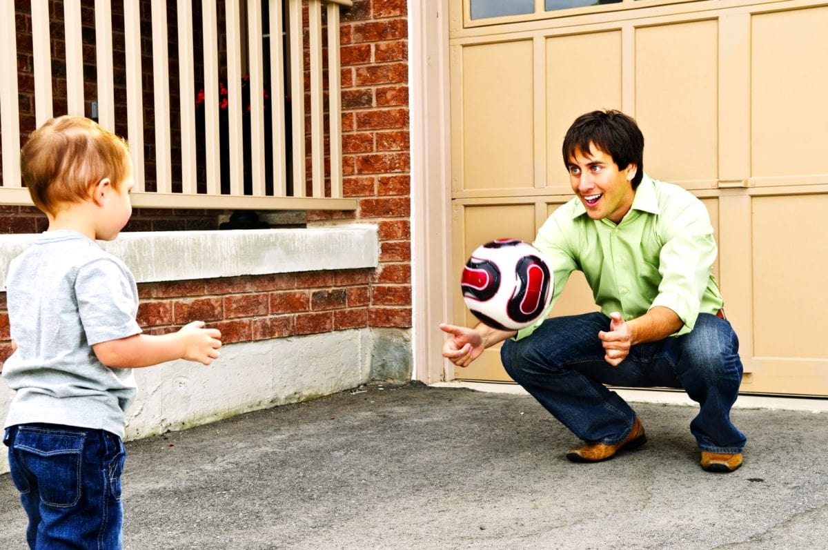 Father teaching son to play soccer on driveway. ○ Soccer Blade