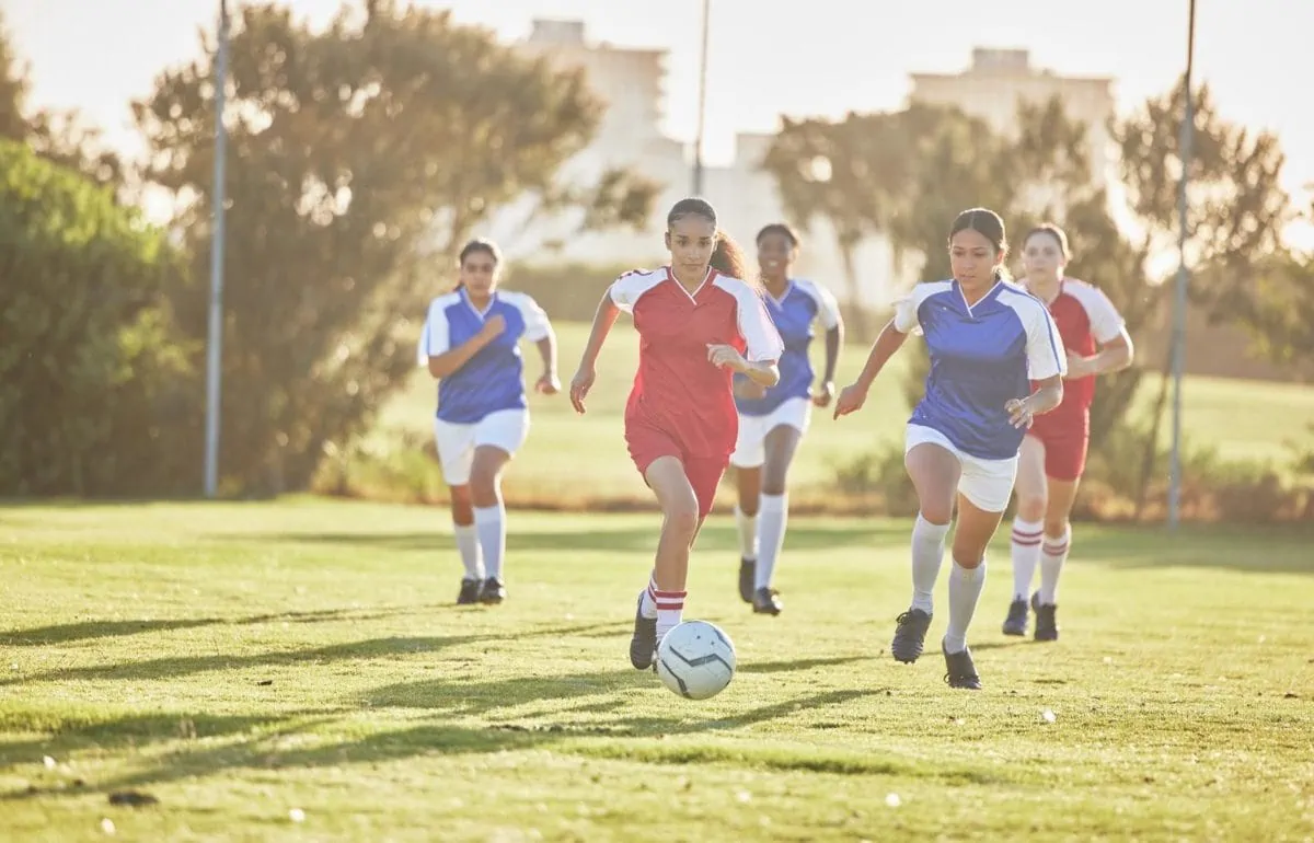 Female soccer team playing a game on a field while passing touching and running with a ball. ○ Soccer Blade