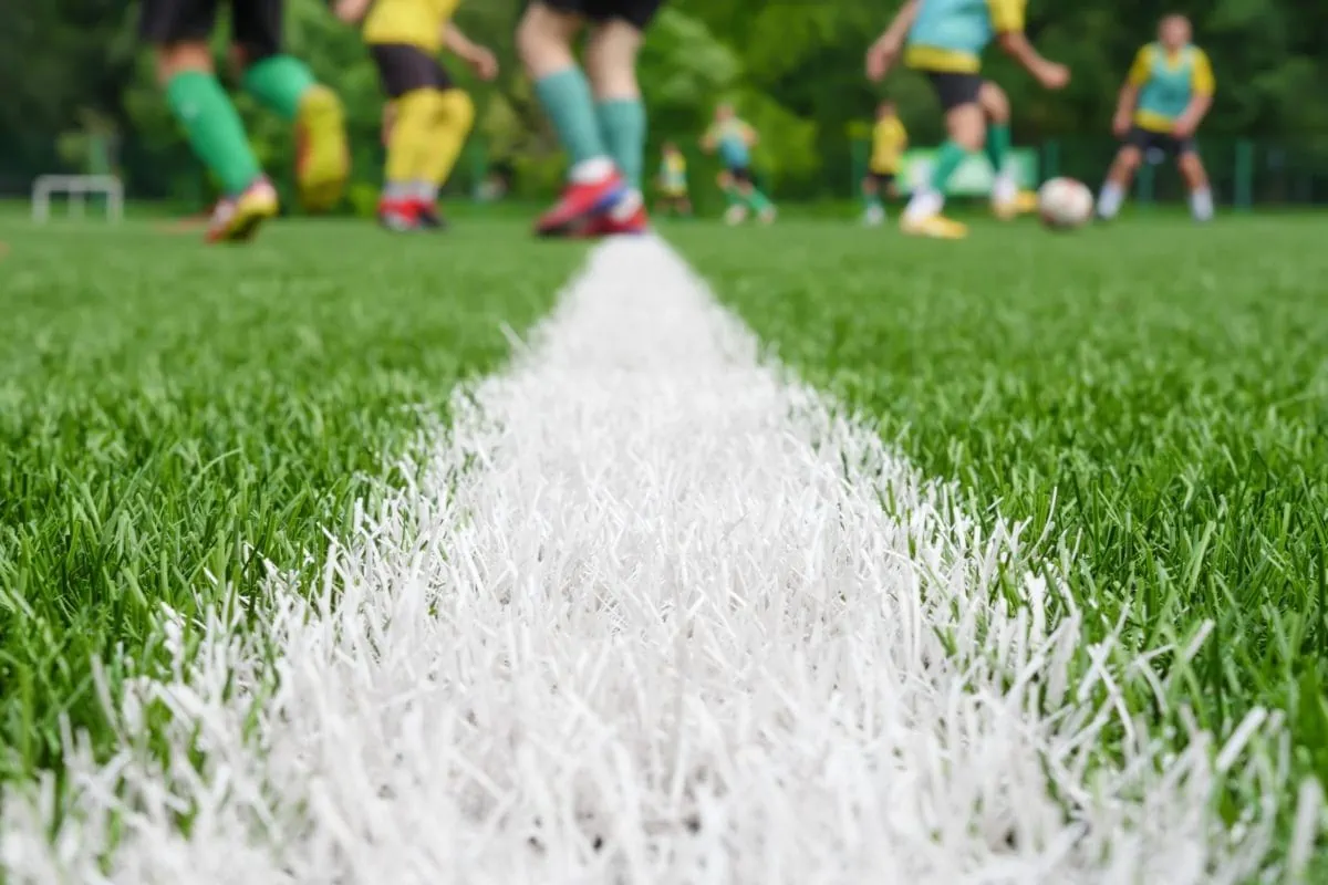 Half way line on a soccer field grass level with players training in the background. ○ Soccer Blade