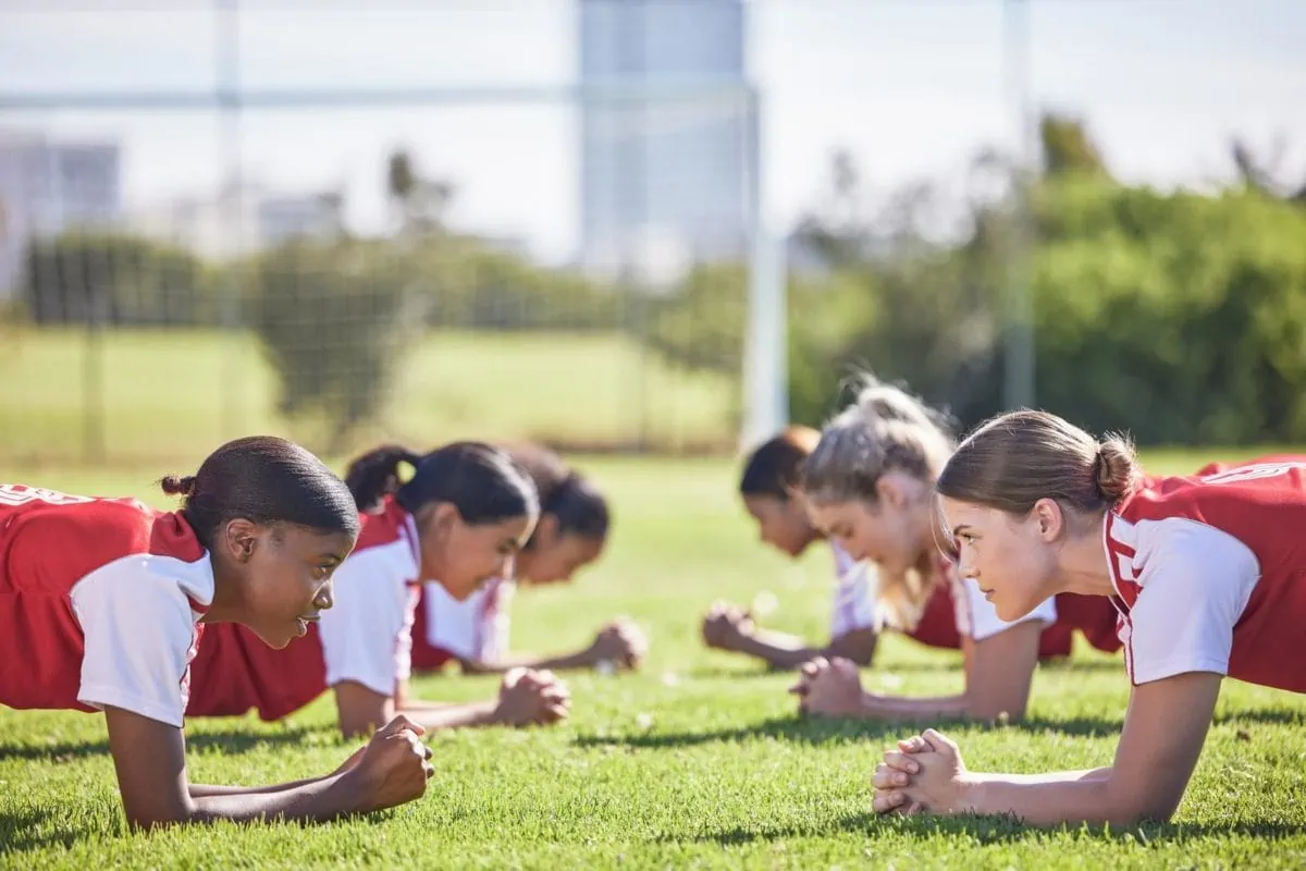 Soccer players doing plank exercise drill girls training team working on a fitness workout. ○ Soccer Blade