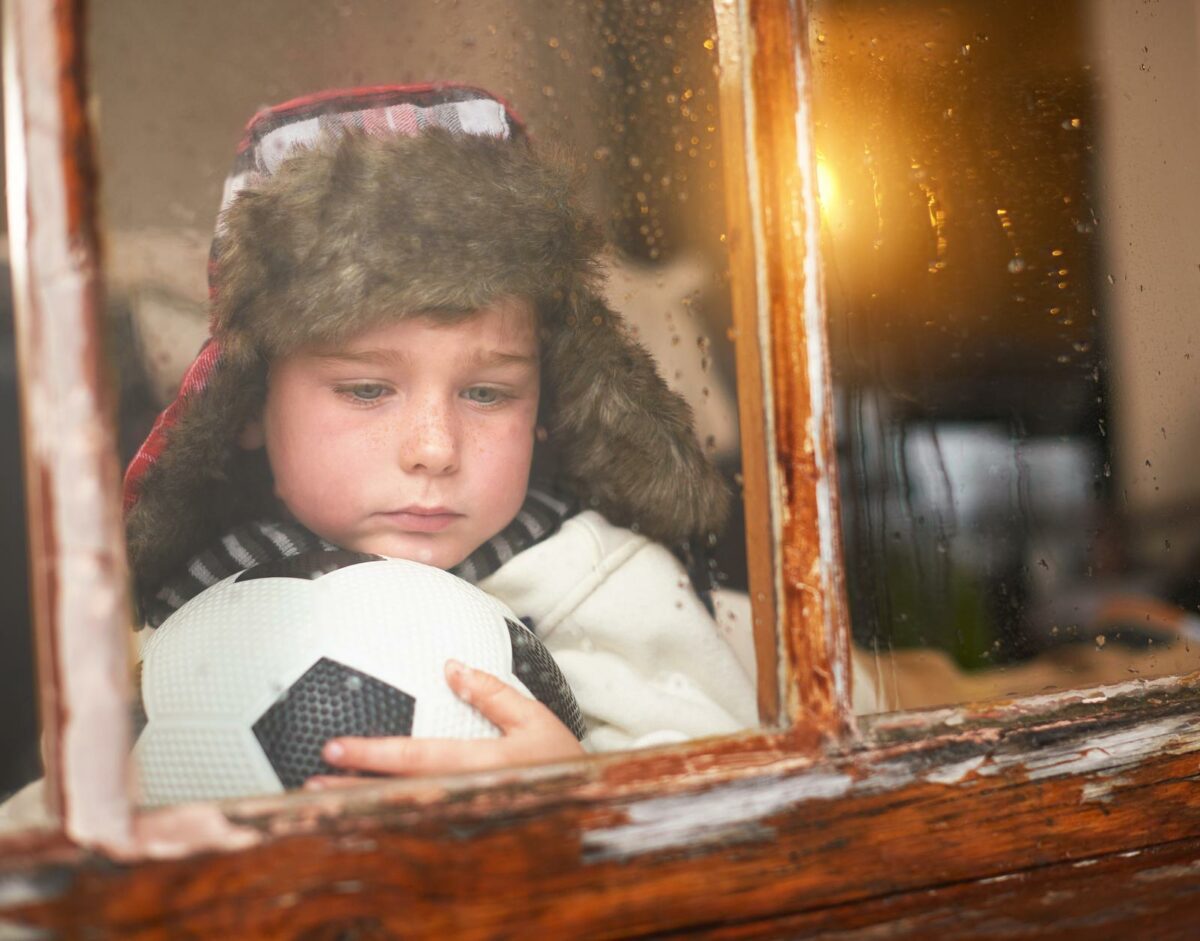 Hes got the rainy day blues. a sad little boy holding a soccer ball while watching the rain through a window ○ Soccer Blade
