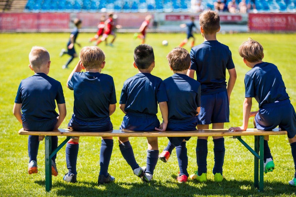 Soccer Match For Children. Young Boys Playing Tournament Soccer Match. Youth Soccer Club Footballers. Young Football Players in Blue Jerseys. Young Soccer Team Sitting on Wooden Bench ○ Soccer Blade