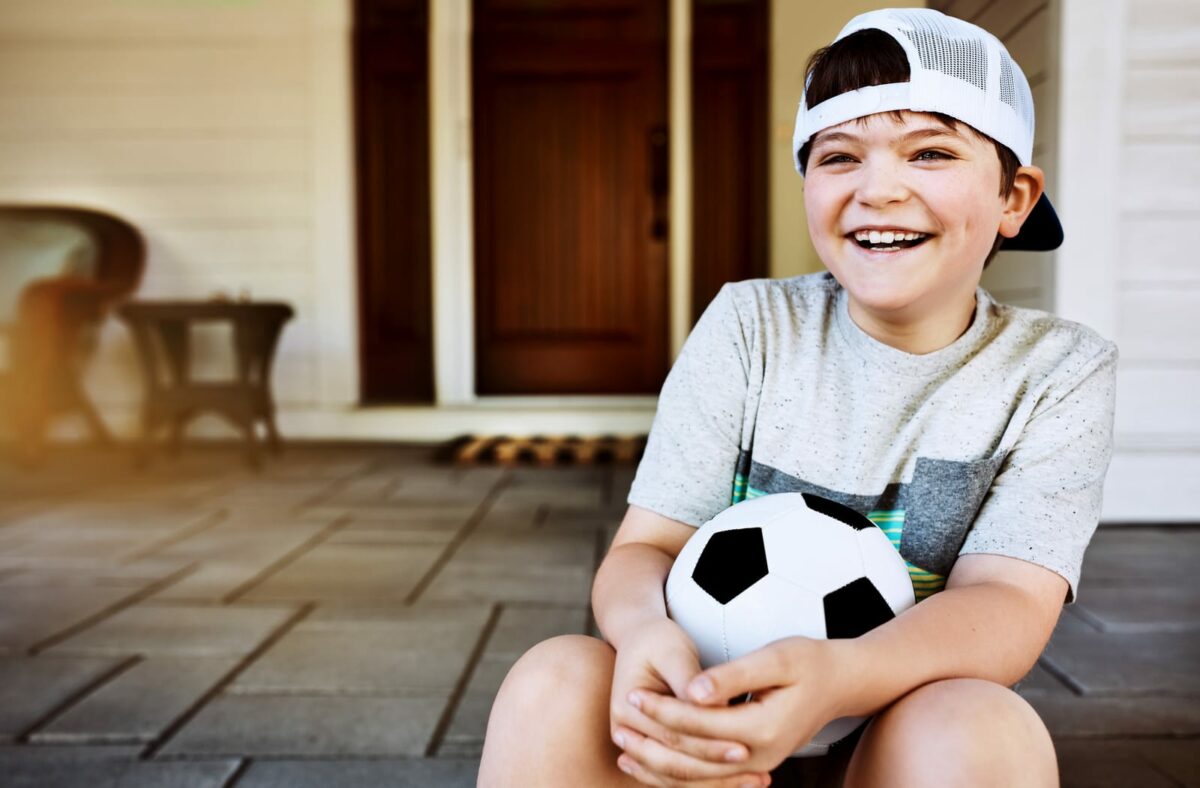 He looks forward to soccer practice. a little boy sitting on the porch with his soccer ball ○ Soccer Blade
