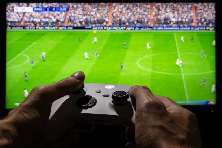 2023 Man playing EA FC 24 with Xbox controller on TV screen ○ Soccer Blade